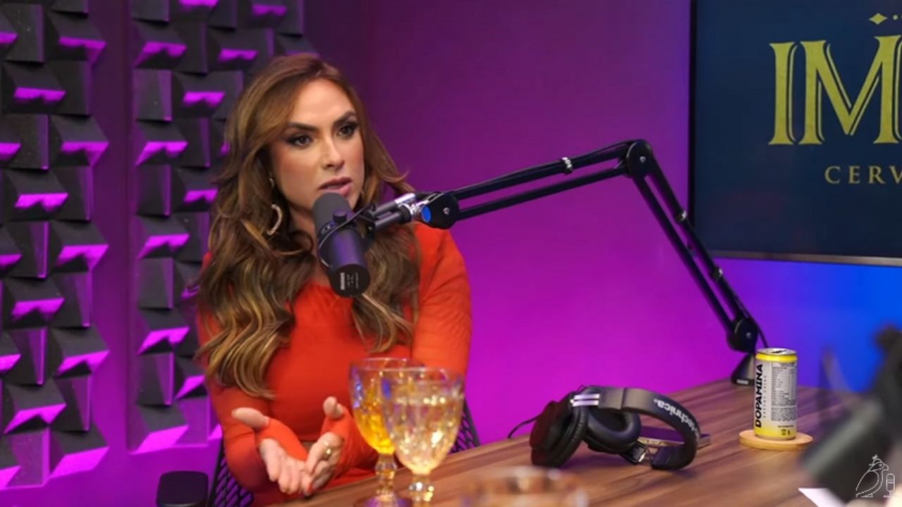 Nicole Bahls de roupa vermelha e cabelos soltos, falando em estúdio de podcast