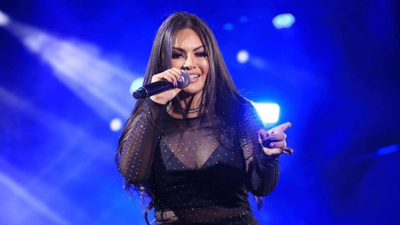 Paulinha Abelha com roupa preta e cabelos soltos, cantando com microfone na mão