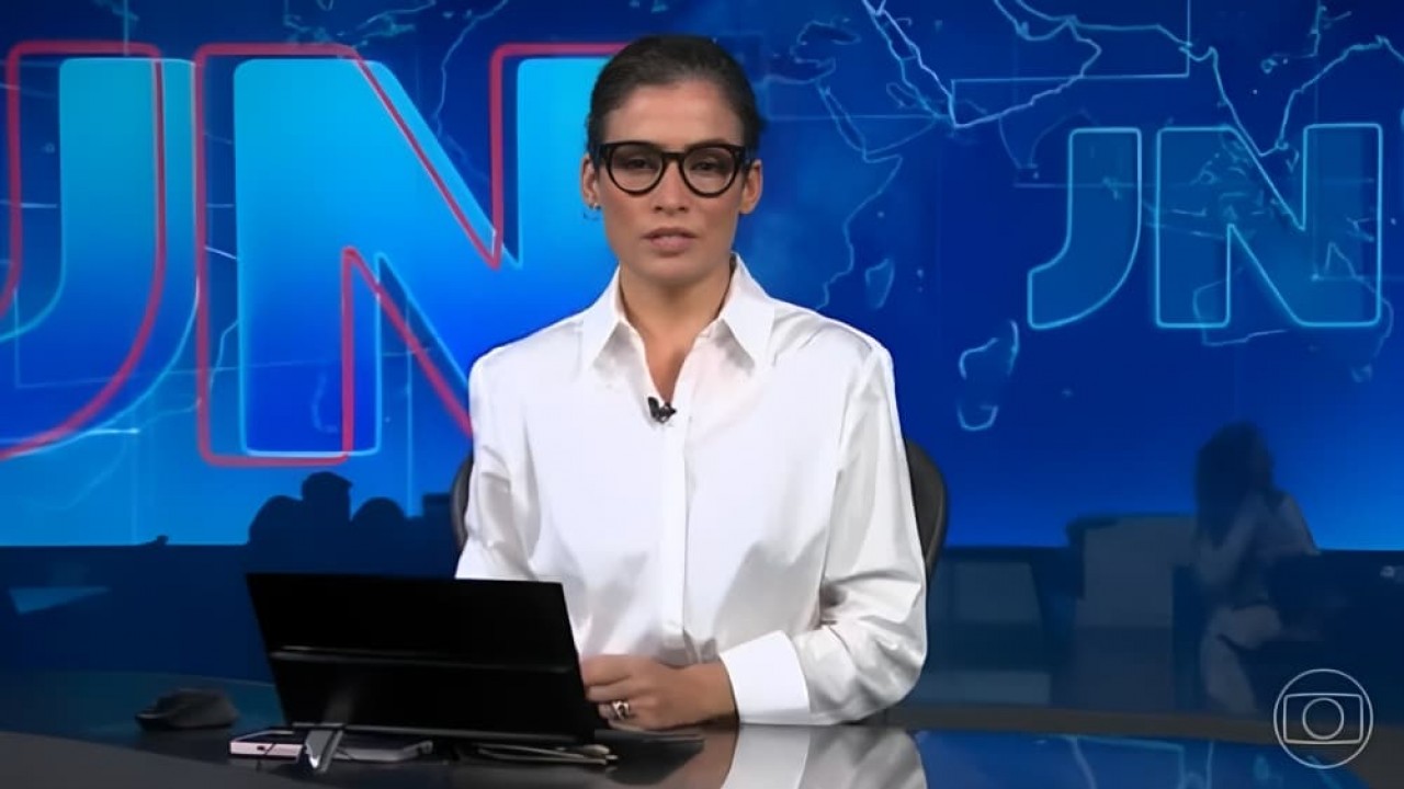 Renata Vasconcellos de camisa branca e cabelo preso na bancada do Jornal Nacional