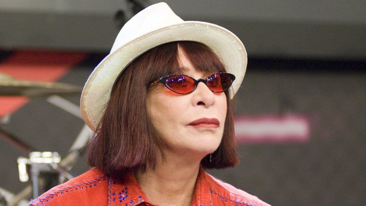 Rita Lee com expressão séria, de chapéu e óculos