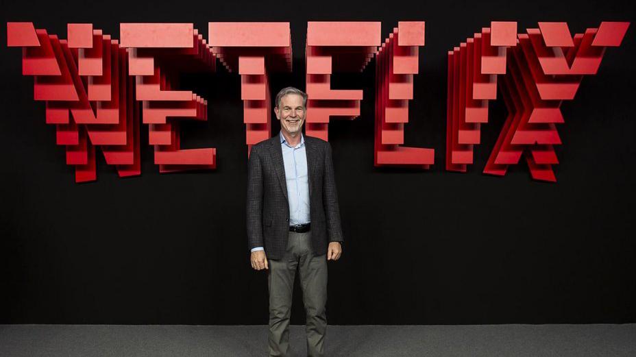 Reed Hastings com o logo da Netflix ao fundo