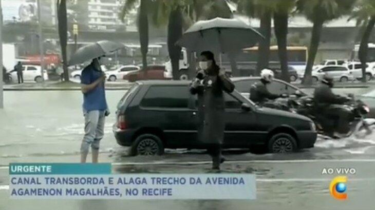 Repórter se encaminha para entrevistas pessoa, durante o alagamento, com guarda-chuva em uma mãe e microfone na outra