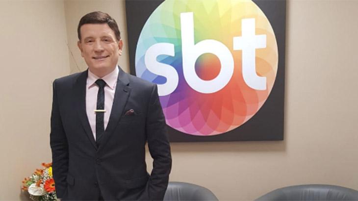 O jornalista Roberto Cabrini posa em frente à logomarca do SBT