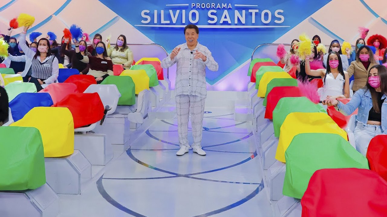 Silvio Santos na volta de seu programa rindo com braços abertos