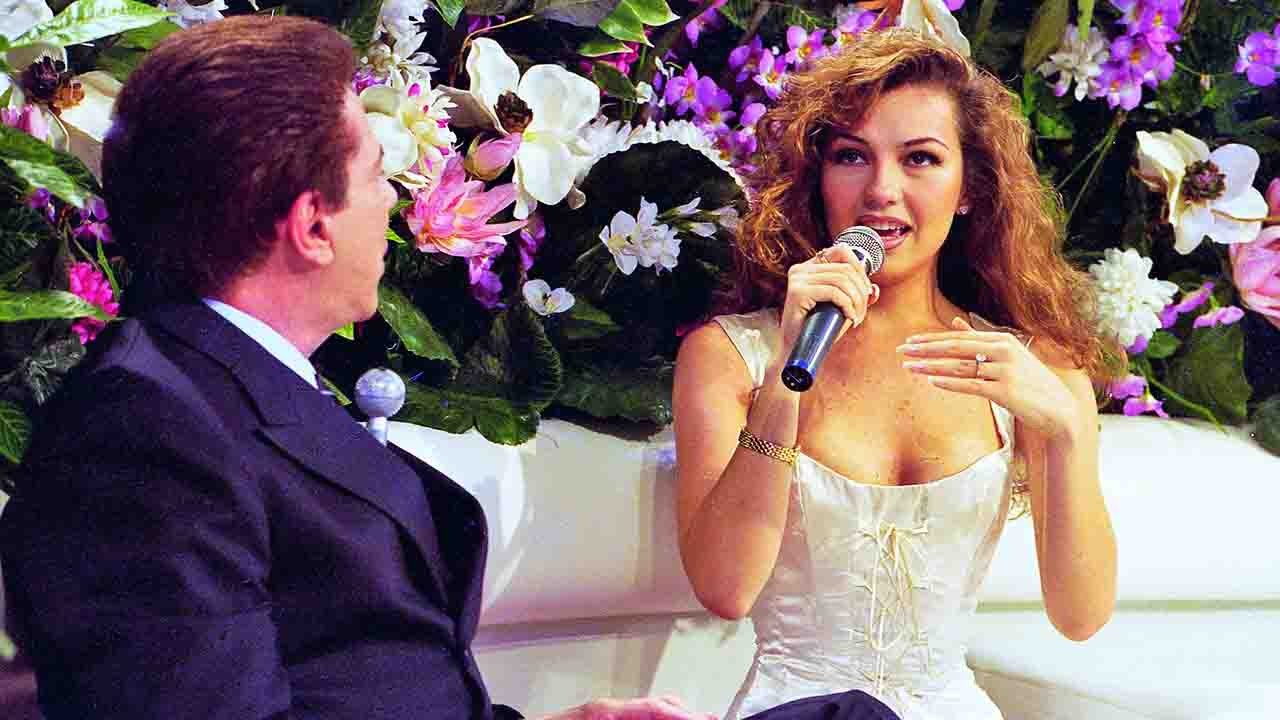Thalía segurando microfone no palco do SBT ao lado de Silvio Santos