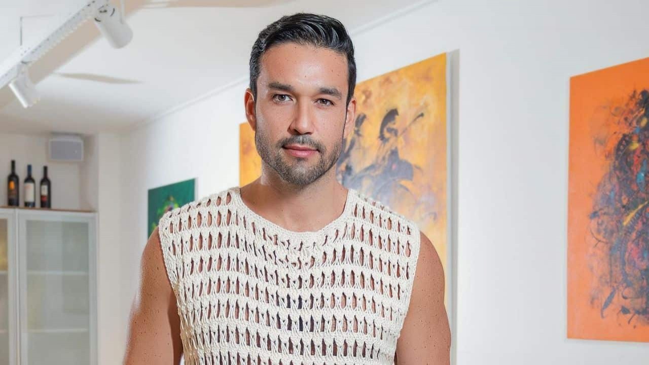 Sergio Marone de camisa clara, perto de quadros coloridos, sem sorrir
