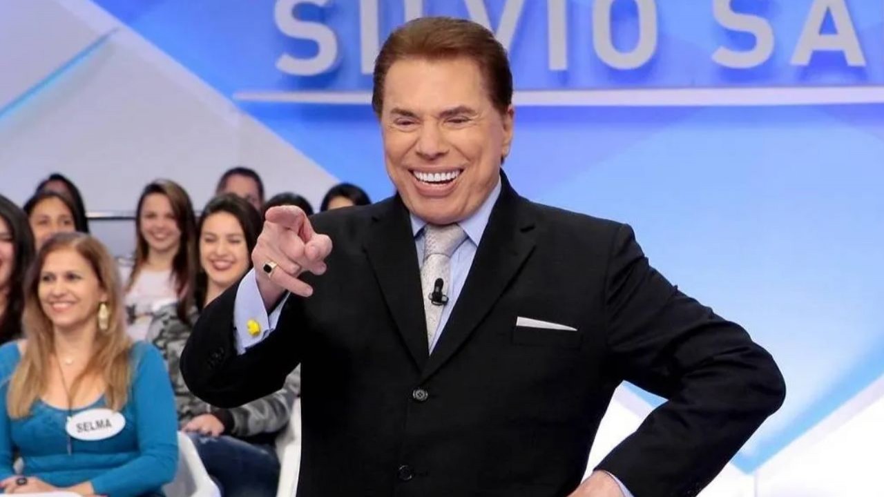 Silvio Santos de terno e gravata, sorrindo e apontando para frente