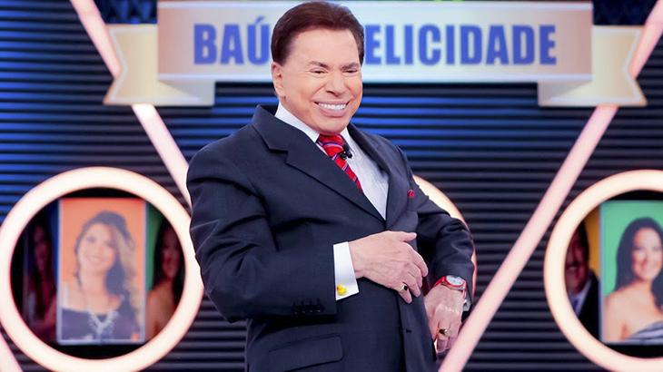 O apresentador Silvio Santos, com terno e gravata, sorri no palco do seu programa no SBT