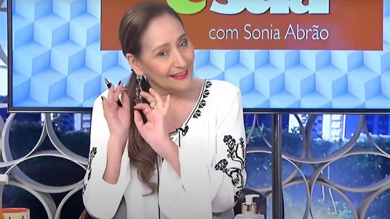 Sonia Abrão falando e gesticulando, de blusa branca e rabo de cavalo