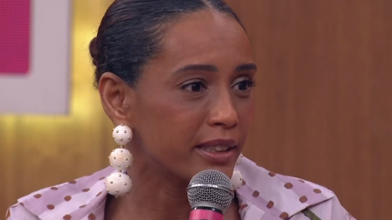 Taís Araujo pede filme das Empreguetes no Encontro, na Globo. A atriz usa uma blusa branca com bolinhas marrons e um brinco com três bolas brancas recheados de bolinhas douradas