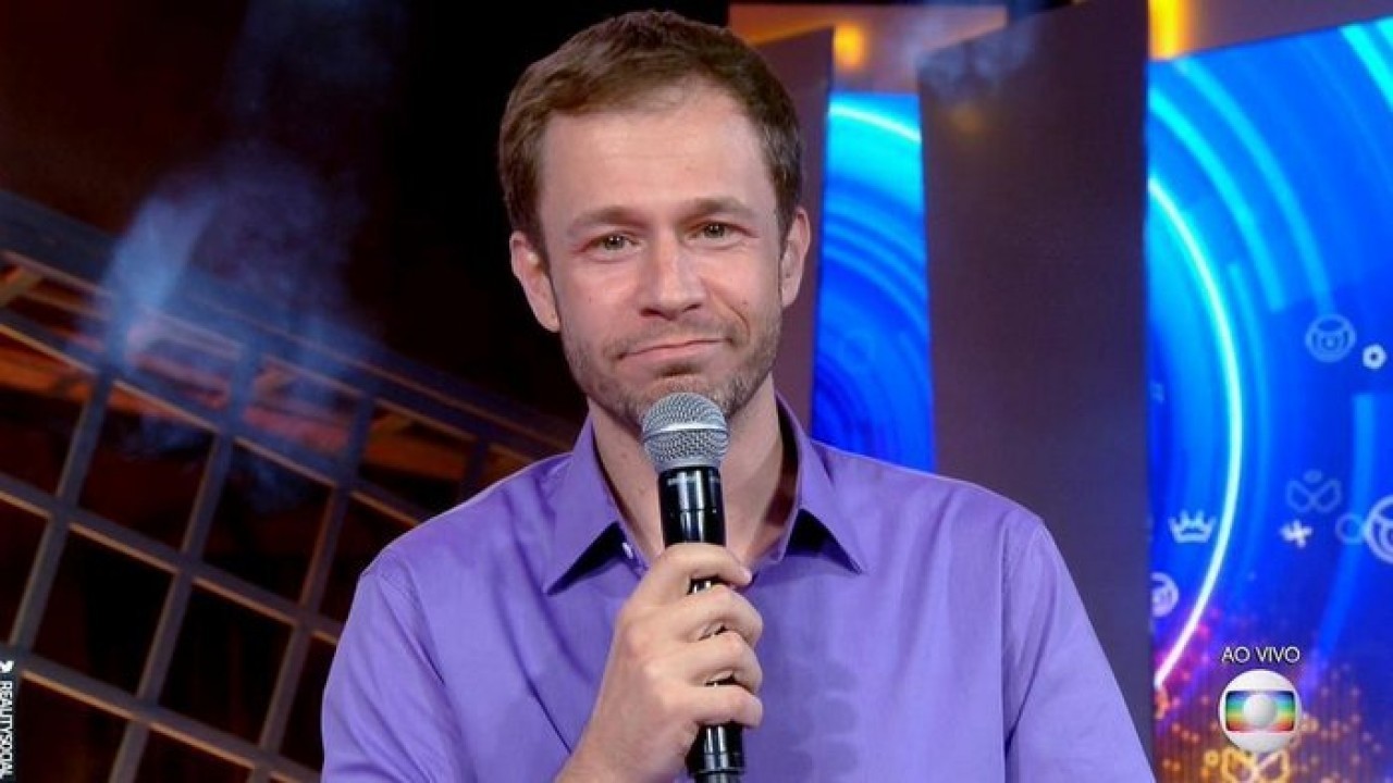 Tiago Leifert de camisa lilás e microfone na mão