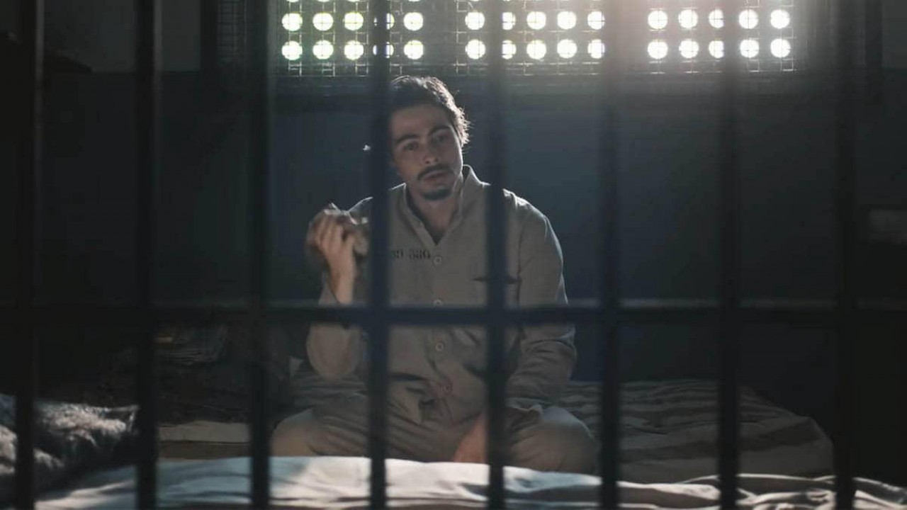 Davi sentado na cama de sua cela em cena de Além da Ilusão