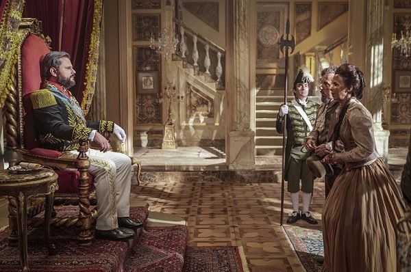 Dom Pedro II sentado no trono enquanto atende Quinzinho e Clemência