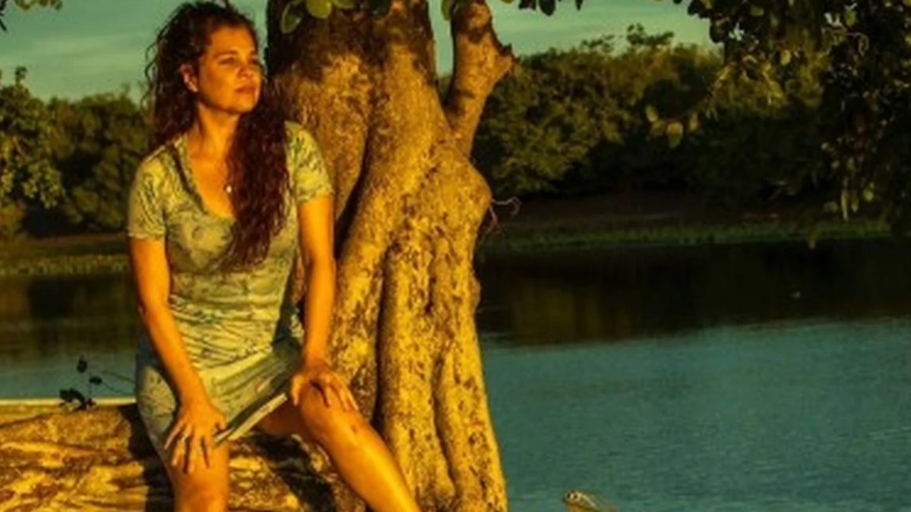 Maria Bruaca sentada na beira do rio em cena de Pantanal