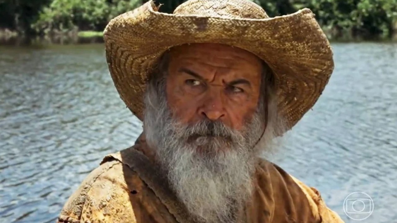 Osmar Prado, como Velho do Rio, usando barbudo e usado chapéu em cena de Pantanal