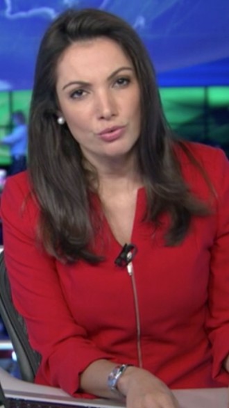 Patrícia Poeta na bancada do Jornal Nacional; jornalista usa camisa social vermelha e olha para câmera de frente