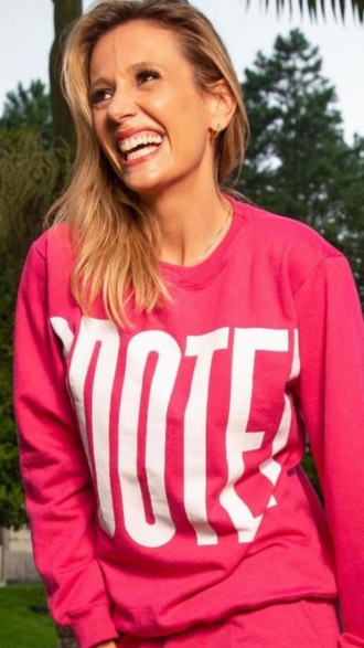 Luísa Mell de moletom cor de rosa com a palavra "adote" escrita em branco; ela sorrindo e olhando para o lado